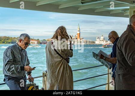 A man reading a newspaper standing next to other passengers on a Vaporetto or water bus service on The Venice Lagoon, on route to Venice ,Italy