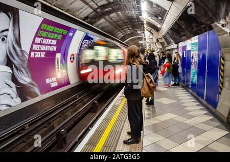 Passengers stand and wait on the platform as a London Underground train pulls into the platform at Bank station