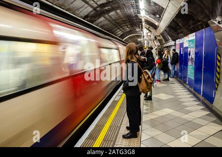 Passengers stand and wait on the platform as a London Underground train pulls into the platform at Bank station Stock Photo