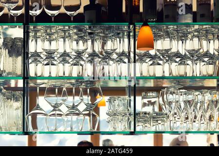 Wall of many empty transparent wine glasses on glass shelf at bar cafe or restaurant against backlit window. Abstract alcoholic beverages pub Stock Photo