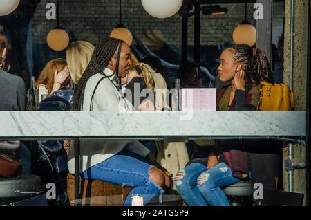 Friends socialise together in a bar in London and sit in the window. Stock Photo