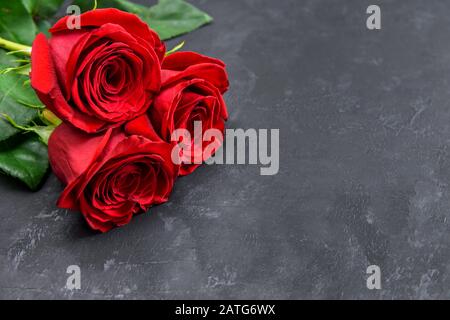 Three red roses on a dark table with copy space for text. Selective focus. Stock Photo