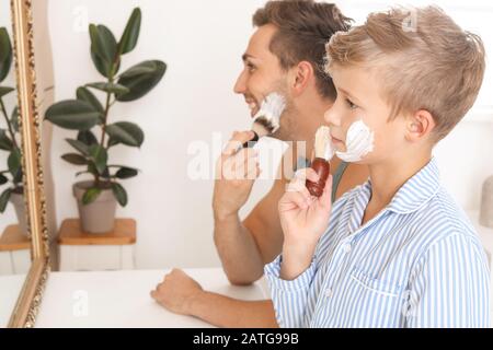 Father with son applying shaving foam onto their faces in bathroom Stock Photo