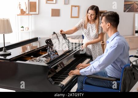 Woman teaching young man in wheelchair to play piano Stock Photo