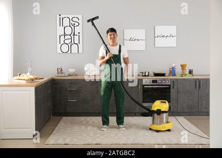 Asian janitor hoovering floor in kitchen Stock Photo