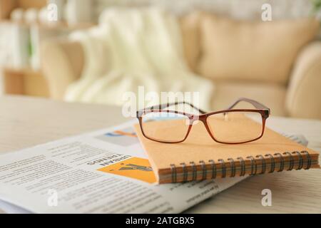 Stylish eyeglasses with newspaper and notebook on table at home Stock Photo