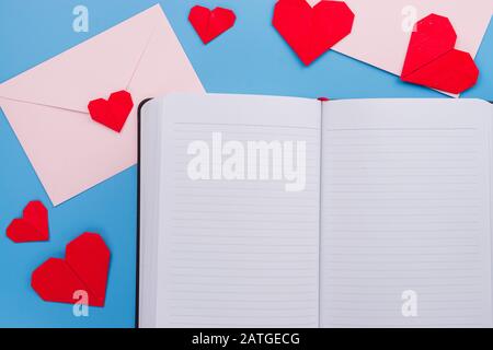 The red paper heart shapes and envelope and notebook over the blue background. Greeting cards, Love and Valentines day concept. Flat lay, top view, co Stock Photo