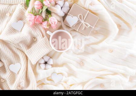 Pink paper hearts with gift box and roses, coffee cup on , beige sweater on cream colour knitted blanket and fluffy background. Love and Valentine's d Stock Photo