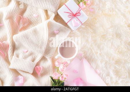 Pink paper hearts with gift box and roses, coffee cup on , beige sweater on cream colour knitted blanket and fluffy background. Love and Valentine's d Stock Photo