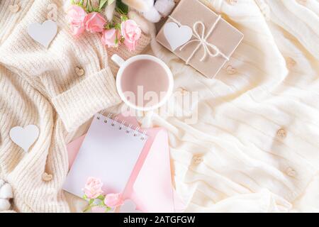 Pink paper hearts with gift box and roses, coffee cup on , beige sweater on cream colour knitted blanket and fluffy background. Love and Valentine's d Stock Photo