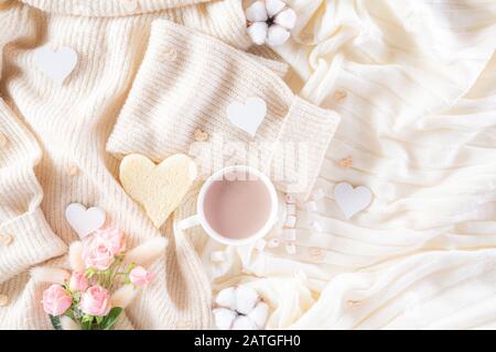 Pink paper hearts with gift box and roses, coffee cup on , beige sweater on cream colour knitted blanket and fluffy background. Love and Valentine's d Stock Photo