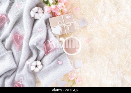 Pink paper hearts with gift box and roses, coffee cup on , beige sweater on cream colour knitted blanket and fluffy background. Love and Valentine's d Stock Photo