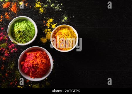 Holi festival celebration. Traditional Indian Holi colours powder decoration with paints. Top view of Organic Gulal colors in bowls, spices, rustic on Stock Photo