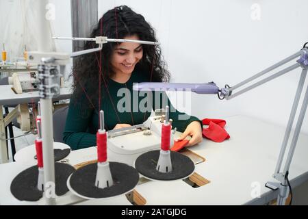 Young woman using professional overlock sewing machine in workshop. Equipment for edging, hemming or seaming clothes at tailors shop Stock Photo
