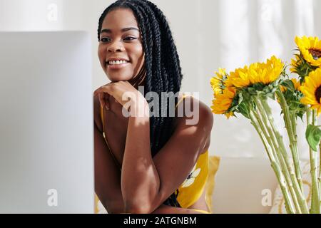 Smiling creative young Black woman working on computer at her desk Stock Photo