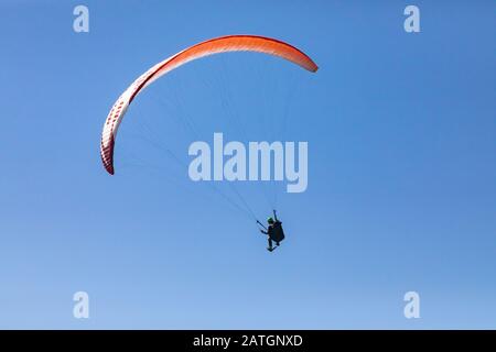 Long shot of flying paraglider against the blue sky. A bright red paraglider flies in the sky. Practicing extremal air sportsman Stock Photo