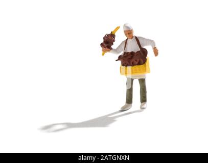 Miniature pretzel seller in white bakers cap and uniform with tray of crispy traditional German pastries around his neck and others displayed on a han Stock Photo