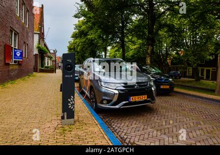 Edam, the Netherlands, August 2019. An Mitsubishi electric car parked and connected to the charging station. The orange cable connected to the car is Stock Photo