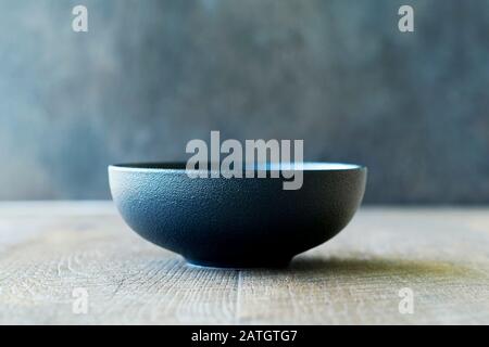 Empty black textured bowl on wooden background. Minimalism. Horizontal orientation. Stock Photo