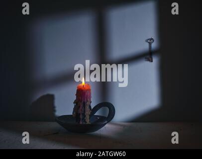 Burning candle against the background of the shadow of the window in the moonlight. A key hangs on the wall. Minimalism. Retro. Stock Photo