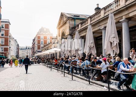 London, UK - May 15, 2019: View of the Covent Garden Market with the restaurant terraces and people sitting. Sunflare on background Stock Photo