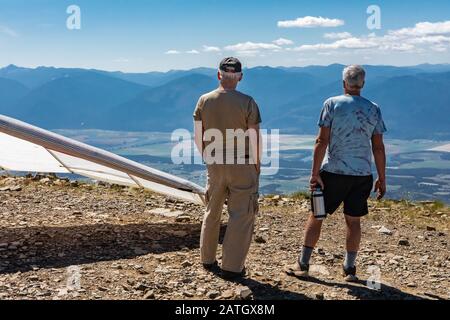 Two people watch hang-glider pilot soaring flight over the Kootenay valley mountains, in Creston, British Columbia, Canada Stock Photo