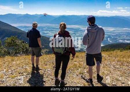Three people watching a hang-glider pilot soaring flight over the Kootenay valley mountains, in Creston, British Columbia, Canada Stock Photo