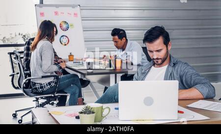 Creative designer director checking work on laptop while team is in casual meeting at background in modern office.agency lifestyle working concept Stock Photo
