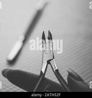 Nippers cuticle scissor in female fingers, cuticle shovel on the blurred background, bw photo. Stock Photo