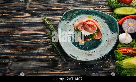 Breakfast. Poached egg, bacon on lettuce made from toast. On a black wooden background. Copy space. Stock Photo