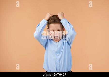 little child boy rips his hair and screams on beige background. Stock Photo