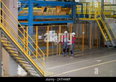 Interracial workers in protective suits standing at fence with control panel and talking about machine in factory shop Stock Photo