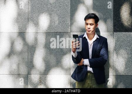 Pensive young handsome businessman reading text messages in his smartphone Stock Photo