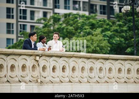 Business team standing on river bridge and enjoying fresh coffee during break Stock Photo