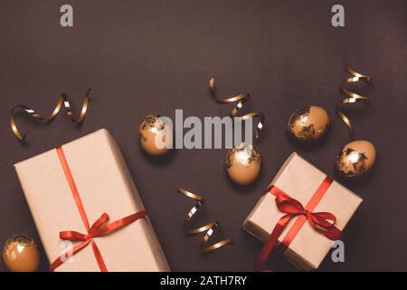 Festive composition of golden eggs and gift box with red ribbon decor on a dark background. Happy easter Stock Photo
