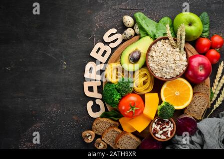 Foods with natural carbohydrates: bread, pasta, avocado, flour, pumpkin, broccoli, beans, spinach. On a brown background. Top view. Free copy space. Stock Photo
