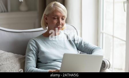 Modern mature woman relaxing at home using laptop Stock Photo