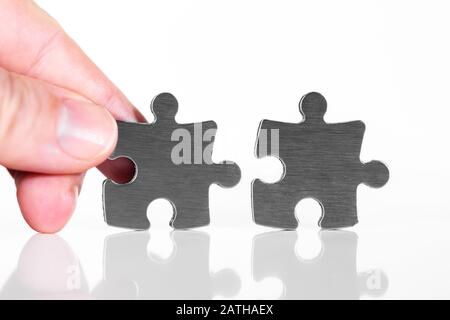 Two puzzle pieces are put together, closeup with male hand, isolated against white background Stock Photo