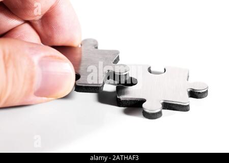 Two puzzle pieces are put together, closeup with male hand, isolated against white background Stock Photo