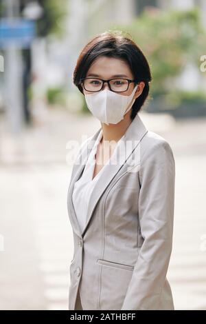 Young Asian businesswoman wearing face mask during epidemic period when walking in city street Stock Photo