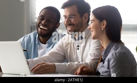 Three multi-ethnic colleagues watching funny prank videos at workplace Stock Photo