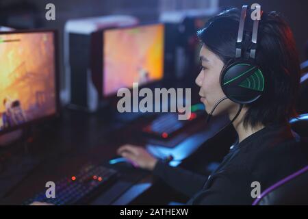 High angle portrait of young Asian man playing videogames and wearing headphones in dark cyber interior, copy space Stock Photo