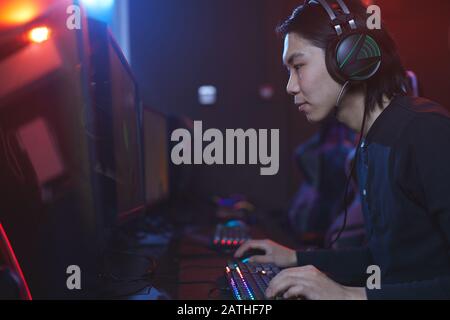 Side view portrait of young Asian man using computer in pro-gaming studio, copy space Stock Photo