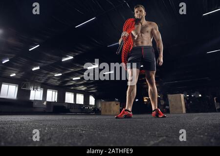 Young healthy man, athlete posing confident with the ropes in gym. Single male model practicing hard and training his upper body. Concept of healthy lifestyle, sport, fitness, bodybuilding, wellbeing. Stock Photo