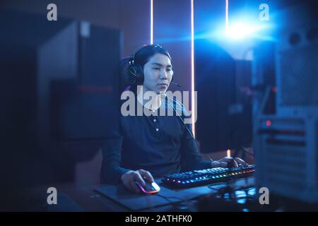 Portrait of young Asian man using computer in dark cyber interior with lens flare, copy space Stock Photo