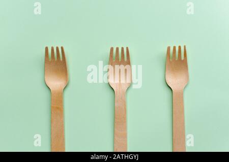 Three single use wooden fork on a green background, environment friendly concept Stock Photo