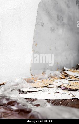 Woodchip wallpaper is removed or scraped off the wall, leftovers lie on the floor on a foil or tarpaulin, concept remodeling or renovation Stock Photo