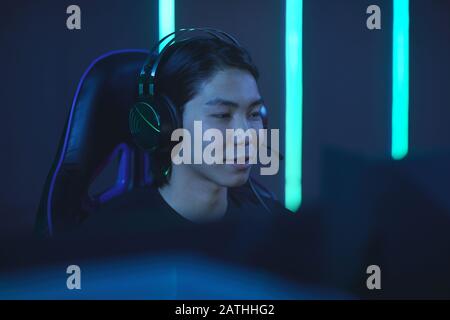 Portrait of smiling Asian man speaking to headset while enjoying videogames in dark room, copy space Stock Photo