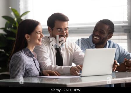 Cheery workers sitting at desk watching funny videos on laptop Stock Photo