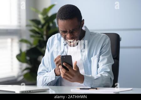 African man holding cellphone shouting feels outraged having gadget problems Stock Photo